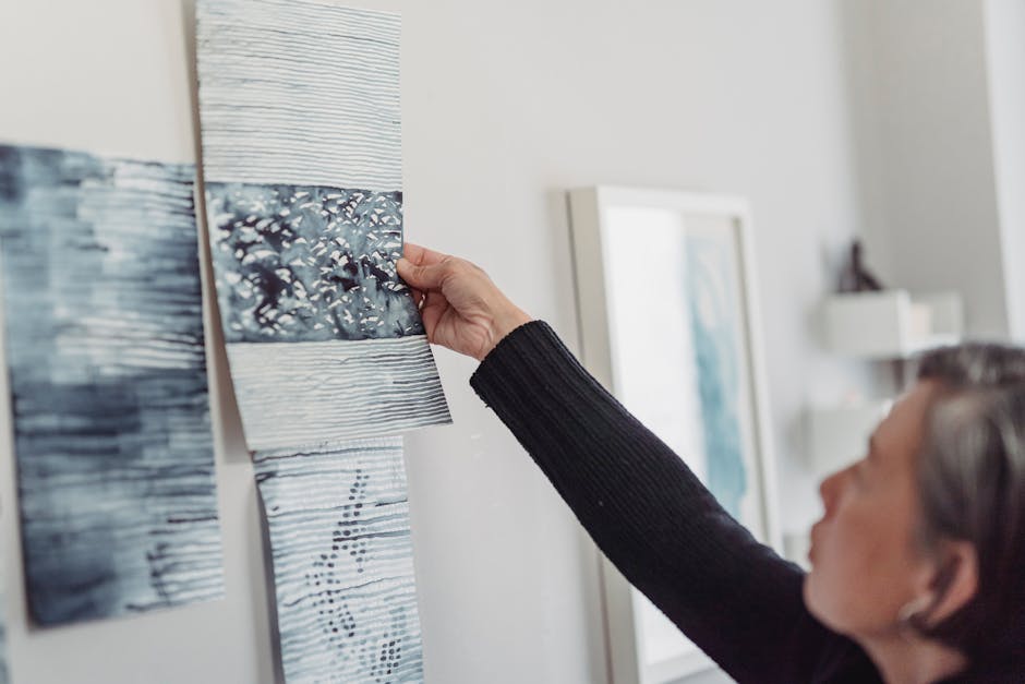A woman arranges abstract paintings on an indoor gallery wall, focusing on creativity.