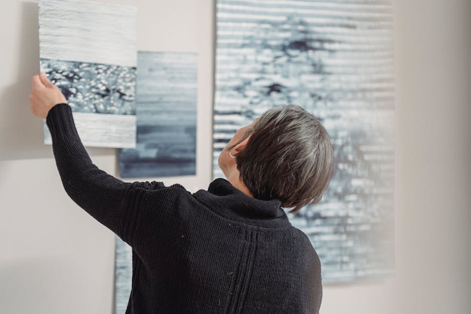 A woman arranges abstract art pieces on a gallery wall, showcasing modern creativity.